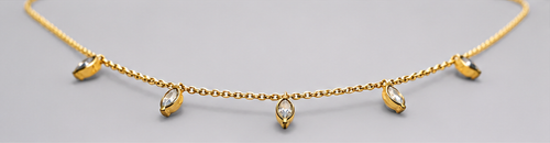 Low-angle view of SEELE gold-tone necklace with five dangling clear crystal charms on a fine chain.