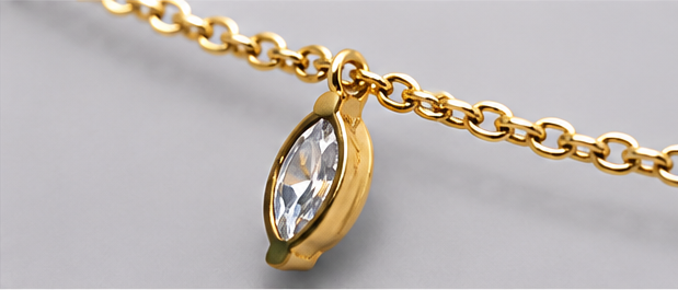 Detailed side-angle close-up of a clear marquise-cut crystal charm in a polished gold-tone setting.