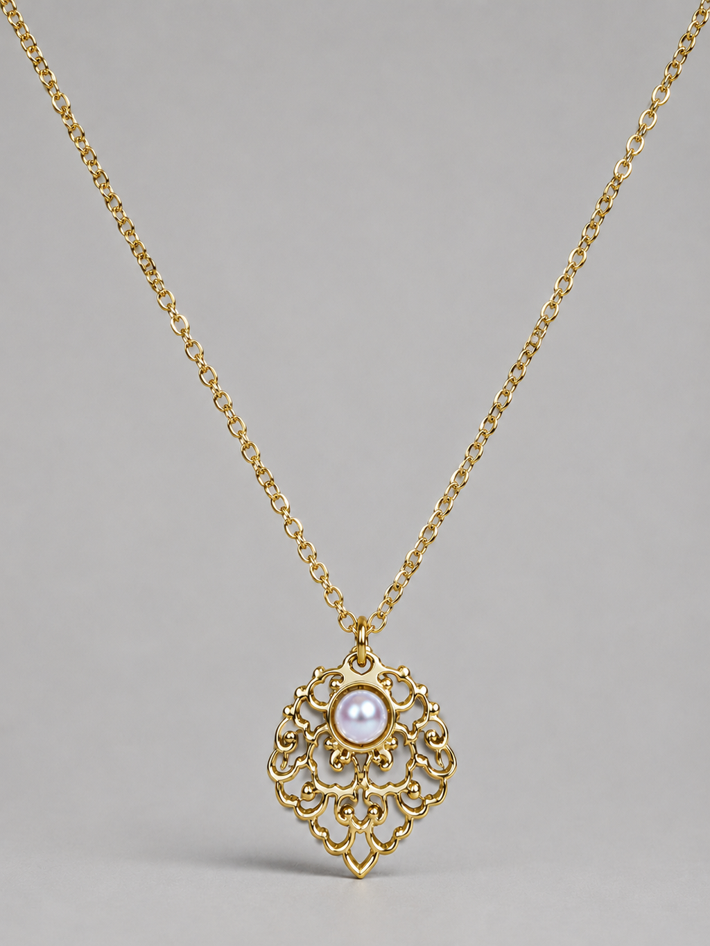 A gold filigree pendant necklace featuring a central white pearl, displayed against a neutral gray background.